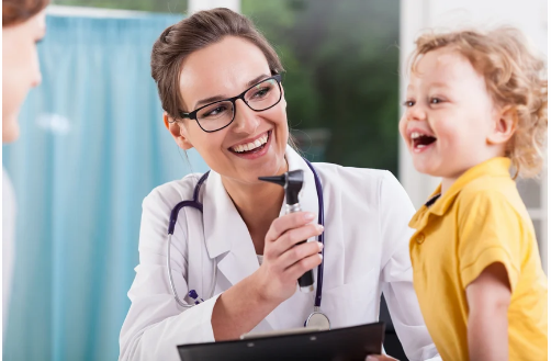 Healthcare professional with exam tool next to smiling child patient