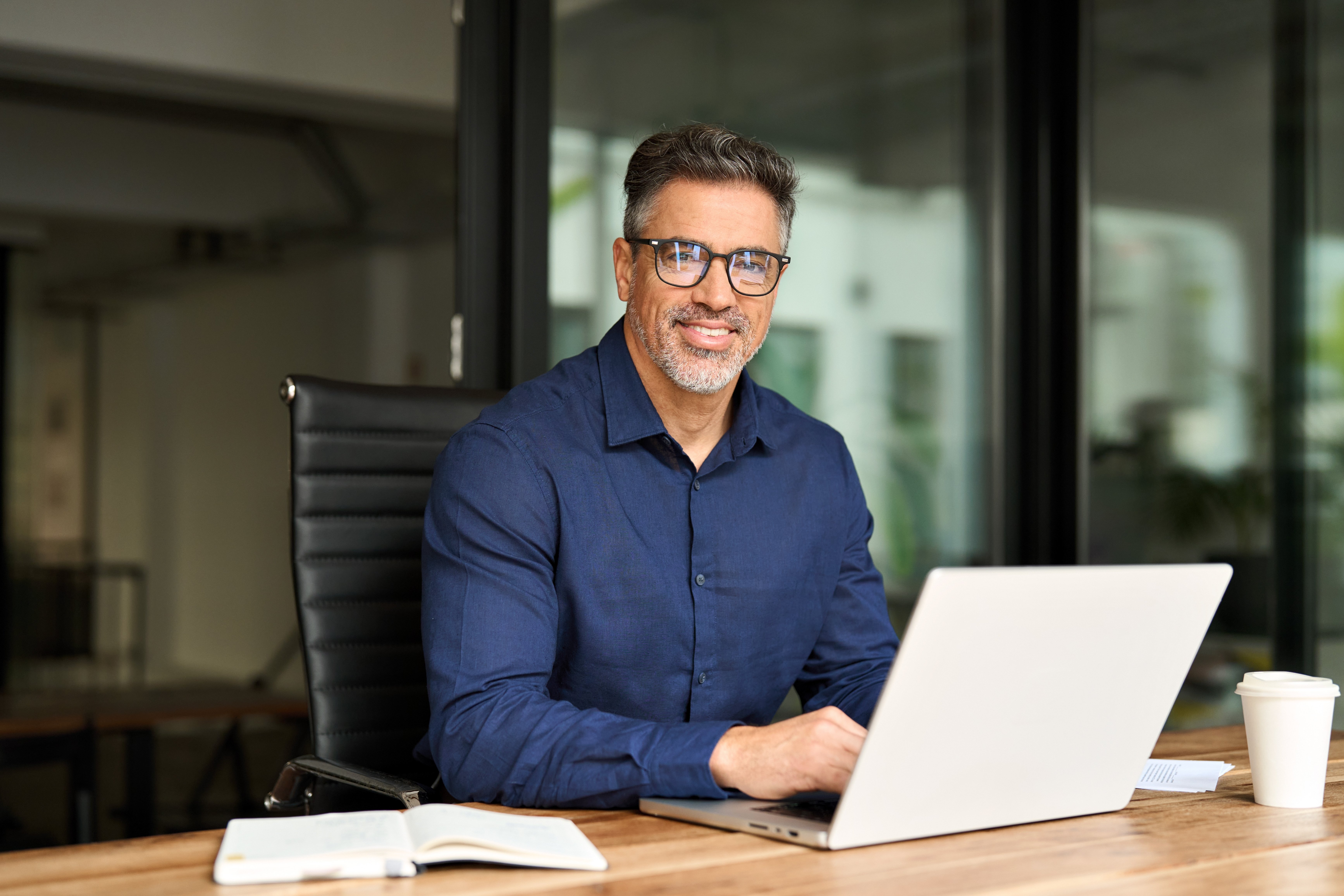 Business_Owner_in_Blue_Button_Up_Shirt_sitting_at_desk_with_a_laptop
